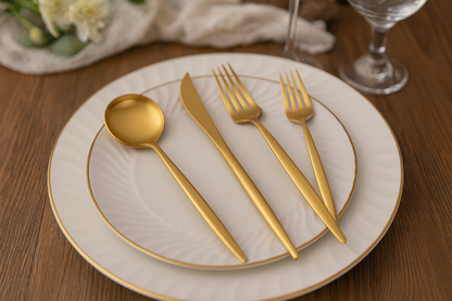 Gold stainless steel cutlery set arranged on white ceramic plates placed on a wooden dining table.”